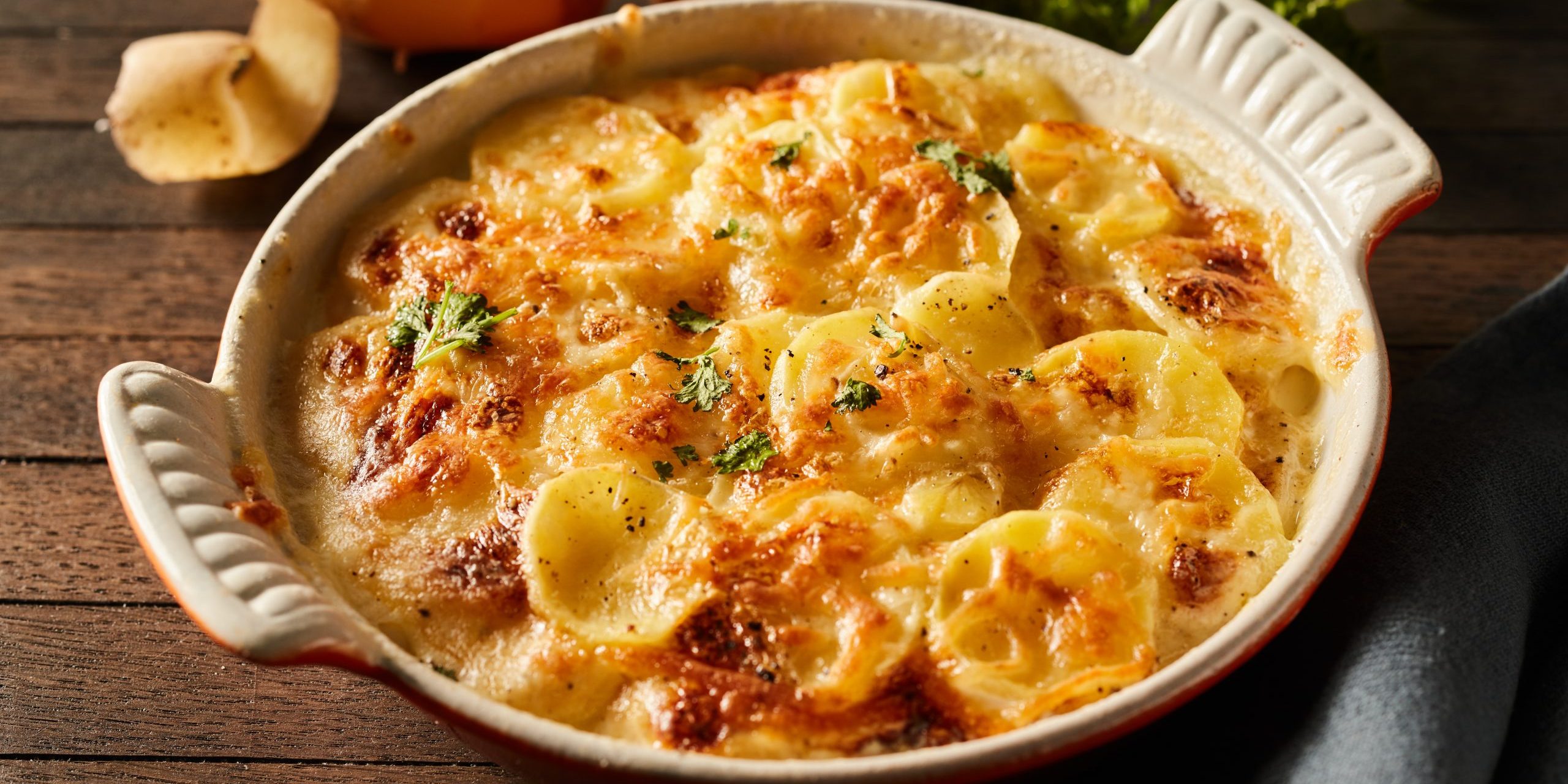 Scalloped gratin potatoes topped with grated cheese and herbs in a ceramic baking dish
